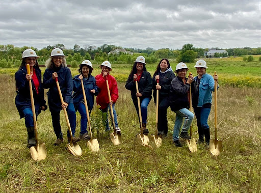 group of people smiling in a field with shovels and hardhats