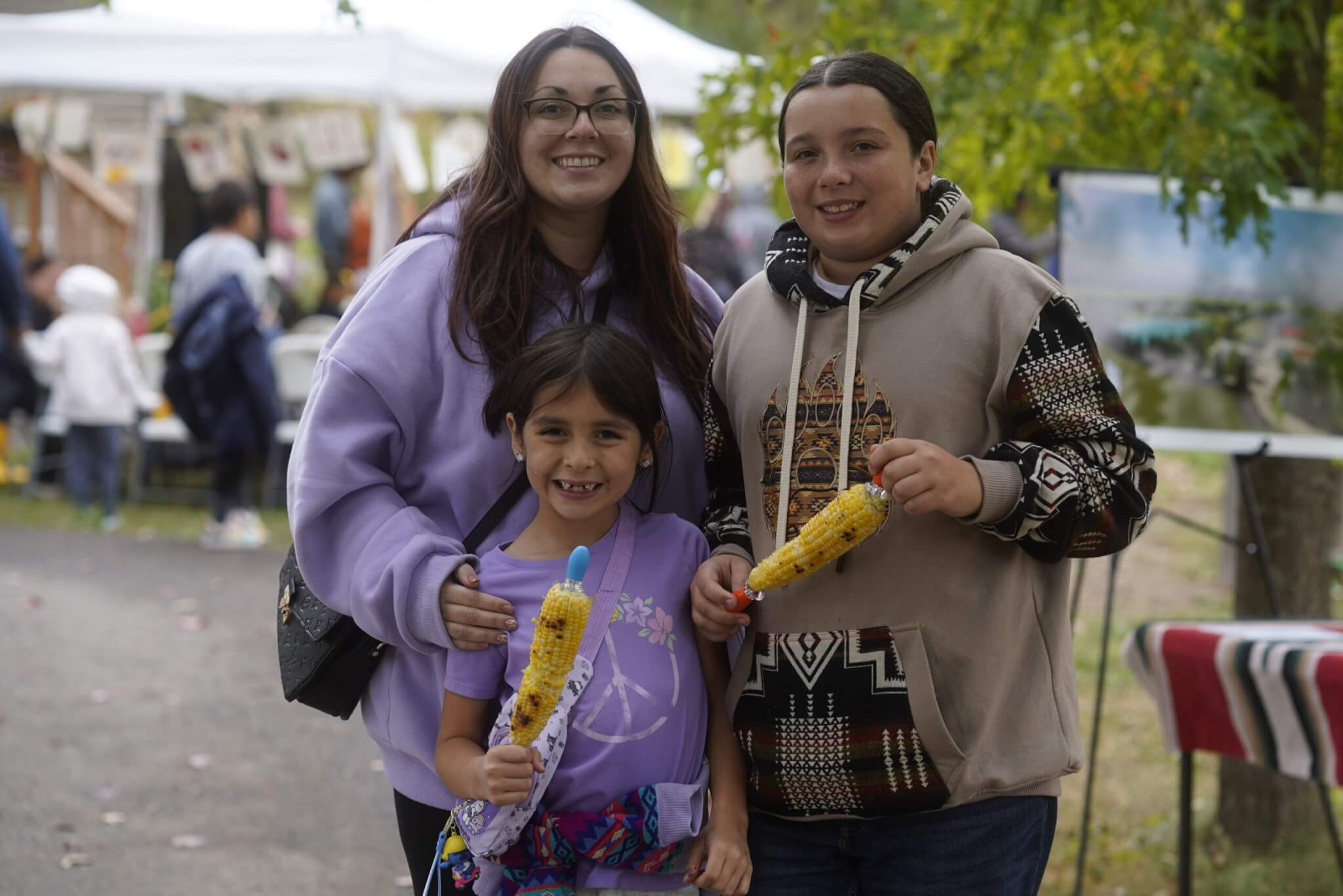 people smiling and holding roasted corn outside